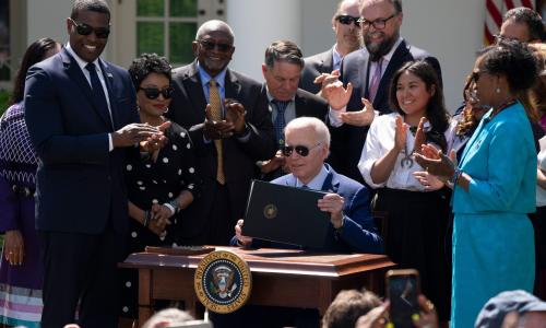 President Biden, surrounded by people, holds an executive order on environmental justice.