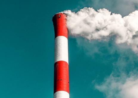 A white-and-red factory chimney with billowing smoke coming out of the top.