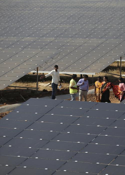 People stand between solar panels installed at the Pavagada Solar Park 175 kilometers (109 miles) north of Bangalore, India.