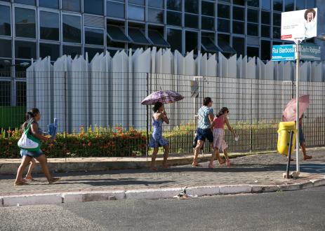 People walking on sidewalk holding umbrellas on a sunny day.