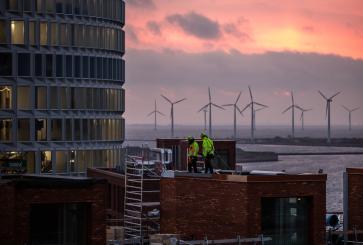 Construction workers on a rooftop with wind turbines. 