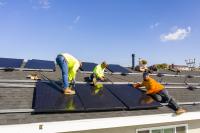 A team of workers install solar panels to a roof in California