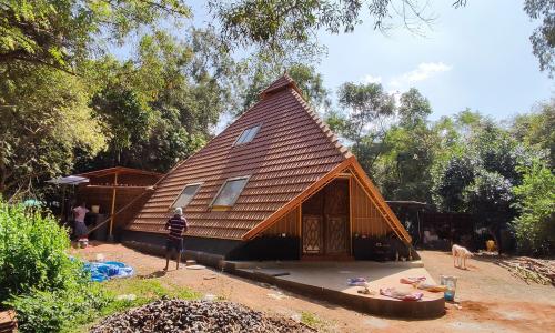 A small A-frame home is constructed in a lush green forested area in India.