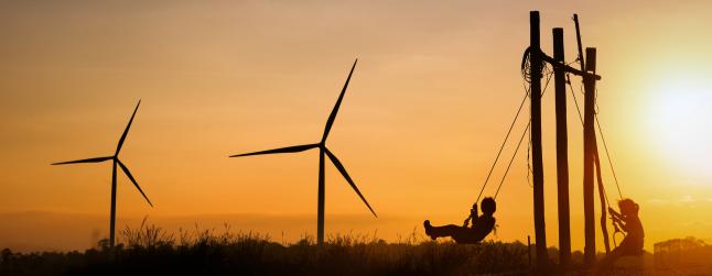 Silhouettes of children playing swing in turbine wind park at sunset