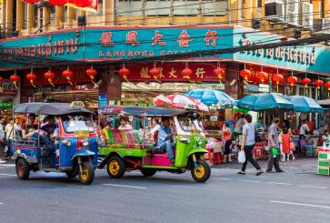 Passengers on a busy Bangkok street ride on colorful three-wheeled tuk-tuks.